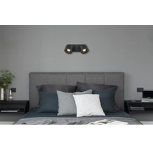 Moderne schwarze Wandleuchte mit zwei Spots über einem grauen Bett in einem Schlafzimmer.
