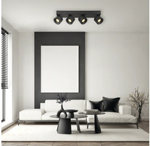 Moderne Deckenleuchte mit vier verstellbaren Strahlern in einem hellen Wohnzimmer mit weißem Sofa und schwarzen Tischen.