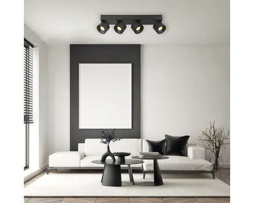 Moderne Deckenleuchte mit vier verstellbaren Strahlern in einem hellen Wohnzimmer mit weißem Sofa und schwarzen Tischen.