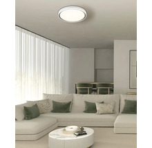 Modernes Wohnzimmer mit runder LED-Deckenleuchte, großem weißem Ecksofa mit grünen Kissen und einem runden Couchtisch aus Marmor.