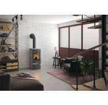 Moderner Kaminofen in Grau in einem Wohnzimmer im industriellen Stil mit weißer Ziegelwand, Sessel und Holzregal.
