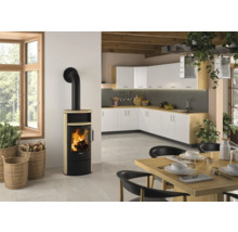 Moderner Kaminofen mit heller Steinverkleidung und schwarzem Ofenrohr in einer hellen Küche mit weißer Küchenzeile und Holztisch.