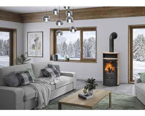 Moderner Kaminofen in einem hellen Wohnzimmer mit grauem Sofa, Holzcouchtisch und winterlichem Ausblick durch ein großes Fenster.
