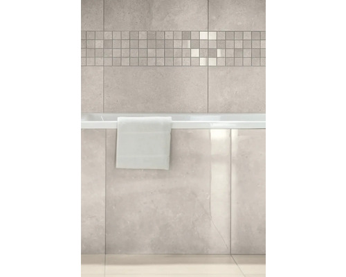 Badezimmer mit hellen Wandfliesen in Steinoptik, einer Mosaikbordüre und einer Badewanne mit glänzender Marmoroptik-Verkleidung.