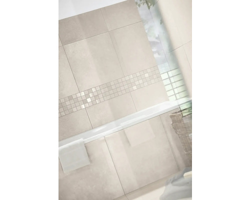 Helles Badezimmer mit großformatigen Wandfliesen in Steinoptik und einer horizontalen Mosaikbordüre über einer weißen Badewanne.
