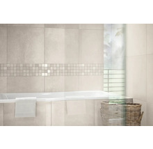 Modernes, helles Badezimmer mit hellen Wandfliesen, Mosaikbordüre, einer weißen Badewanne mit Handtuch und einem Flechtkorb.
