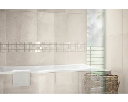 Modernes, helles Badezimmer mit hellen Wandfliesen, Mosaikbordüre, einer weißen Badewanne mit Handtuch und einem Flechtkorb.
