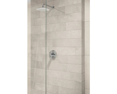 Moderne Dusche mit verchromtem Regenduschkopf, Einhebelmischer und hellgrauen Wandfliesen in Steinoptik hinter einer Glaswand.