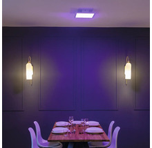 Modernes Esszimmer mit quadratischem LED-Deckenpanel in Lila und zwei Wandleuchten vor einer dunklen Wand mit gedecktem Holztisch und weißen Stühlen.