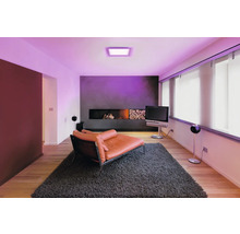Modernes Wohnzimmer mit quadratischem LED-Panel an der Decke, das violettes Licht spendet, orangefarbene Liege auf grauem Teppich.