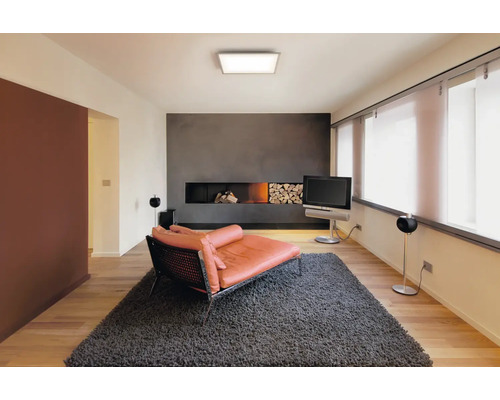 Quadratisches LED Panel an der Decke eines modern eingerichteten hellen Wohnzimmers mit Kamin und Teppich.