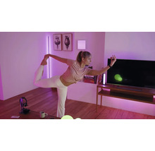 Eine Person macht Yoga in einem Wohnzimmer mit violetter Smart-Home-Beleuchtung, TV-Möbel und Wanddekoration.