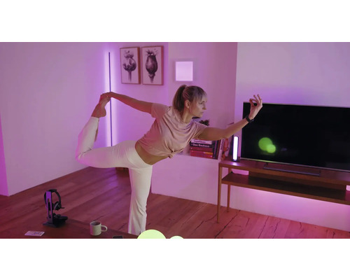 Eine Person macht Yoga in einem Wohnzimmer mit violetter Smart-Home-Beleuchtung, TV-Möbel und Wanddekoration.