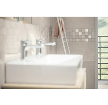 Modernes Badezimmer mit weißem Waschbecken, verchromten Armaturen und Wandfliesen in Steinoptik mit Mosaikbordüre.