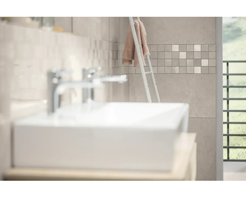 Modernes Badezimmer mit weißem Waschbecken, verchromten Armaturen und Wandfliesen in Steinoptik mit Mosaikbordüre.