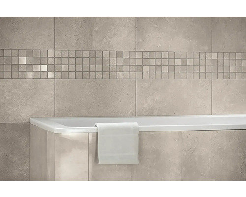 Wandfliesen in Steinoptik mit einer Mosaikbordüre über einer Badewanne mit einem Handtuch in einem hellen Badezimmer.