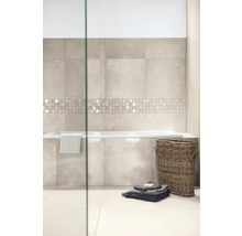 Modernes Badezimmer mit Wandfliesen in hellgrauer Steinoptik, Mosaikbordüre, eingebauter Badewanne, Flechtkorb und Handtüchern auf hellem Fliesenboden.