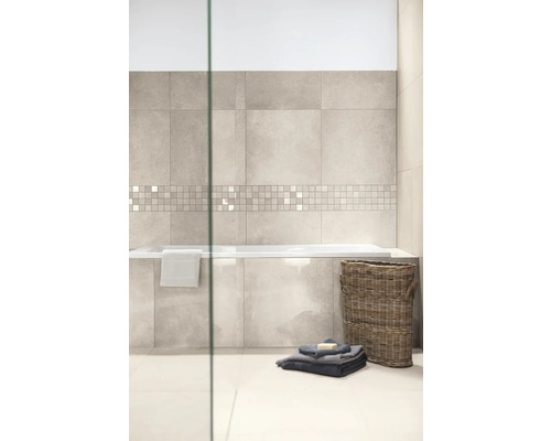 Modernes Badezimmer mit Wandfliesen in hellgrauer Steinoptik, Mosaikbordüre, eingebauter Badewanne, Flechtkorb und Handtüchern auf hellem Fliesenboden.