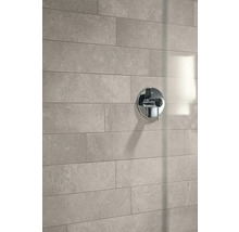 Moderne Badezimmerwand mit rechteckigen Fliesen in Natursteinoptik und einer runden Duscharmatur aus Chrom.