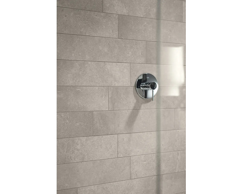 Moderne Badezimmerwand mit rechteckigen Fliesen in Natursteinoptik und einer runden Duscharmatur aus Chrom.