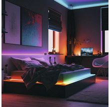 Modernes Schlafzimmer mit smarter LED-Streifen-Beleuchtung unter dem Bett, an der Wand und Decke, erzeugt farbenfrohe Lichteffekte.