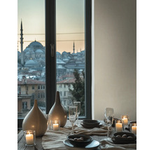 Gedeckter Tisch mit Keramikvasen, Gläsern und Kerzen vor einem Fenster mit Blick auf eine Stadt mit Moscheen bei Dämmerung.