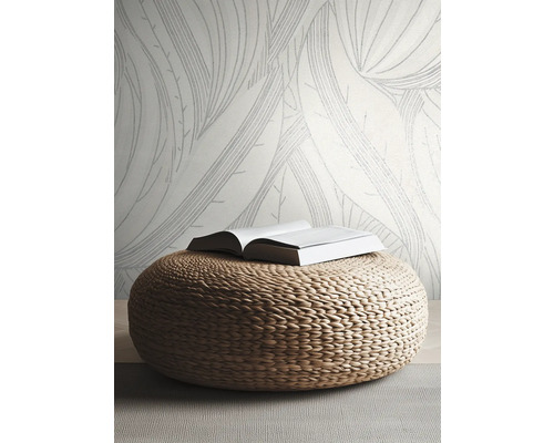 Vliestapete mit großem Blattmuster in hellem, modernem Zimmer mit geflochtenem Sitzpouf aus Naturmaterial.