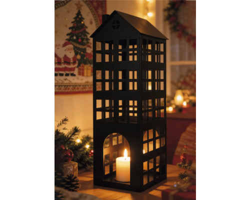 Schwarze Metalllaterne in Hausform mit brennender weißer Kerze in festlicher Weihnachtsumgebung mit Tannenzweigen und warmen Lichterketten.