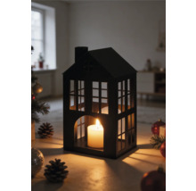 Laterne in Hausform aus schwarzem Metall mit brennender Kerze, umgeben von Weihnachtsdekoration und Tannenzapfen in einem hellen Raum.