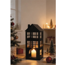Schwarze Metall-Laterne in Hausform mit brennender Kerze in einer weihnachtlichen Szene mit geschmücktem Tannenbaum und Geschenken.