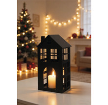 Schwarzes Windlicht in Hausform mit brennender Kerze im weihnachtlich dekorierten Wohnzimmer mit beleuchtetem Weihnachtsbaum.