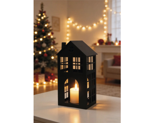 Schwarzes Windlicht in Hausform mit brennender Kerze im weihnachtlich dekorierten Wohnzimmer mit beleuchtetem Weihnachtsbaum.