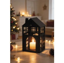 Schwarzes Windlicht in Hausform aus Metall mit brennender Kerze in einem hellen Wohnzimmer mit Weihnachtsbaum und Lichterketten.