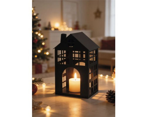 Schwarzes Windlicht in Hausform aus Metall mit brennender Kerze in einem hellen Wohnzimmer mit Weihnachtsbaum und Lichterketten.