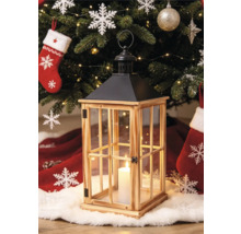 Holzlaterne mit Glasfenstern und schwarzem Metalldach vor einem geschmückten Weihnachtsbaum mit brennender Kerze im Inneren.