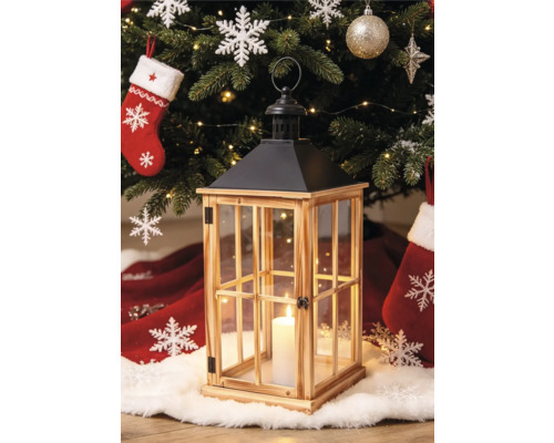 Holzlaterne mit Glasfenstern und schwarzem Metalldach vor einem geschmückten Weihnachtsbaum mit brennender Kerze im Inneren.