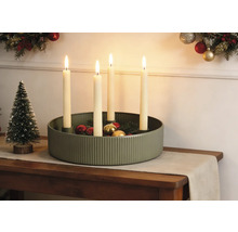 Festliche Weihnachtsdekoration mit gerippter grüner Metallschale, vier brennenden Kerzen, Weihnachtskugeln und einem kleinen Dekobaum auf einem Tisch.