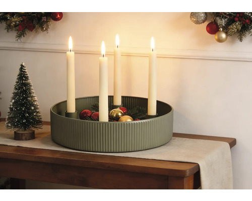 Festliche Weihnachtsdekoration mit gerippter grüner Metallschale, vier brennenden Kerzen, Weihnachtskugeln und einem kleinen Dekobaum auf einem Tisch.