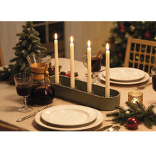 Adventsleuchter mit vier brennenden Stabkerzen auf einem festlich gedeckten Weihnachtstisch mit Geschirr und Dekoration.
