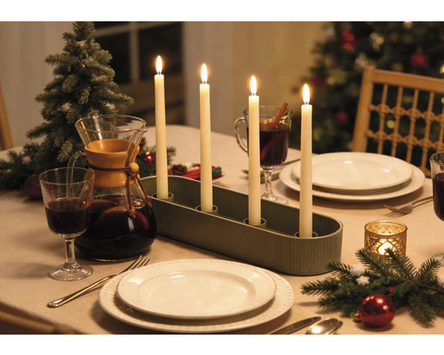 Adventsleuchter mit vier brennenden Stabkerzen auf einem festlich gedeckten Weihnachtstisch mit Geschirr und Dekoration.
