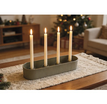 Ovaler grüner Kerzenhalter mit vier brennenden weißen Stabkerzen auf einem Läufer in einem weihnachtlich dekorierten Wohnzimmer.