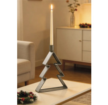 Kerzenständer aus Metall in Weihnachtsbaumform mit brennender Stabkerze auf einem Tisch in einem festlich dekorierten Wohnzimmer.