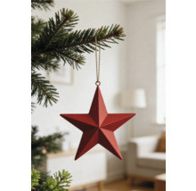 Roter Weihnachtsanhänger Stern aus Metall an einem Tannenzweig in einem hellen Raum.