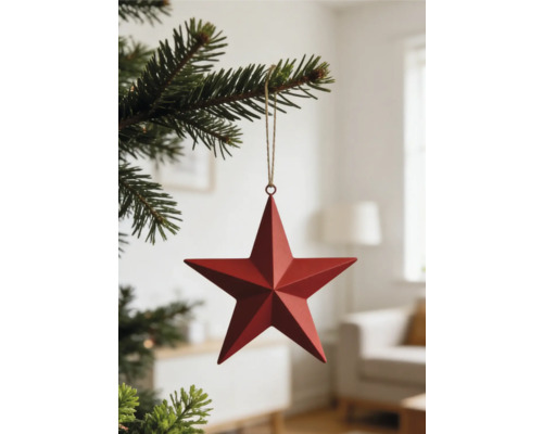 Roter Weihnachtsanhänger Stern aus Metall an einem Tannenzweig in einem hellen Raum.