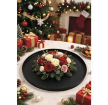 Weihnachtliches Blumengesteck mit Rosen, Tannenzweigen und Zapfen auf einem schwarzen Tablett vor einem festlich geschmückten Weihnachtsbaum.