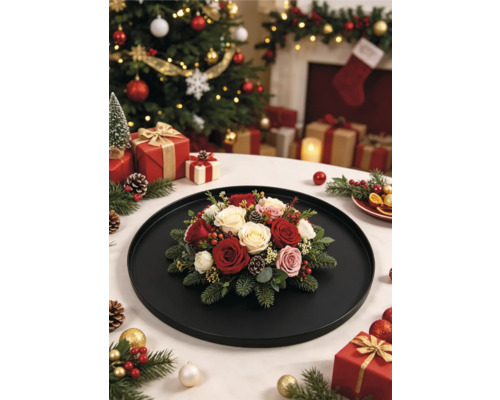 Weihnachtliches Blumengesteck mit Rosen, Tannenzweigen und Zapfen auf einem schwarzen Tablett vor einem festlich geschmückten Weihnachtsbaum.