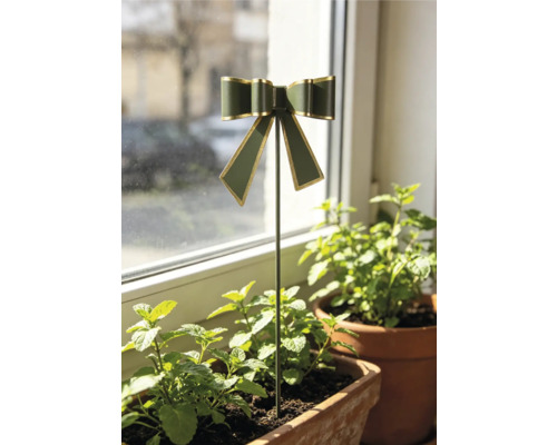 Dekorativer Blumenstecker mit Schleife in Dunkelgrün und Gold, platziert in einem Kräutertopf aus Ton auf einer Fensterbank.