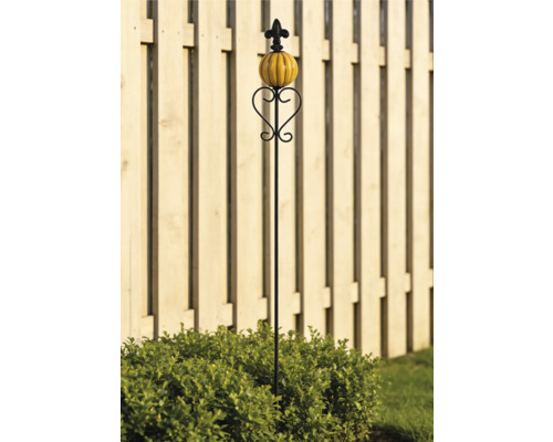 Schwarzer Gartenstecker aus Metall mit Herz-Ornament, orangefarbenem Keramik-Kürbis und Lilie vor einem Holzzaun.