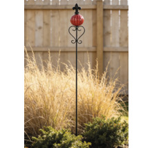 Dekorativer Gartenstab aus Metall mit einer roten Keramikkugel und einer Lilienverzierung in einem Garten mit Ziergras.