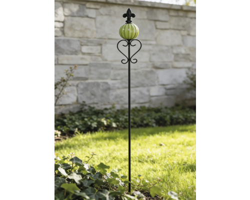 Schwarzer Beetstecker aus Metall mit grüner Glaskugel und Lilienverzierung auf einer Rasenfläche.